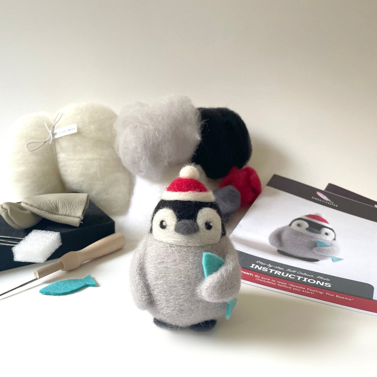 Plush penguin toy with crafting tools and materials on a white surface