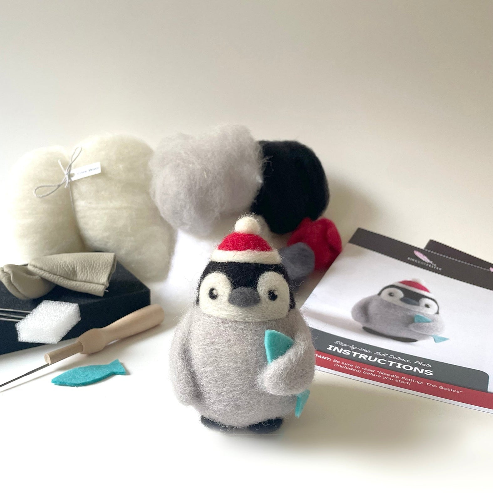 Plush penguin toy with crafting tools and materials on a white surface