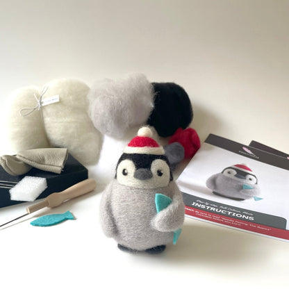 Plush penguin toy with crafting tools and materials on a white surface