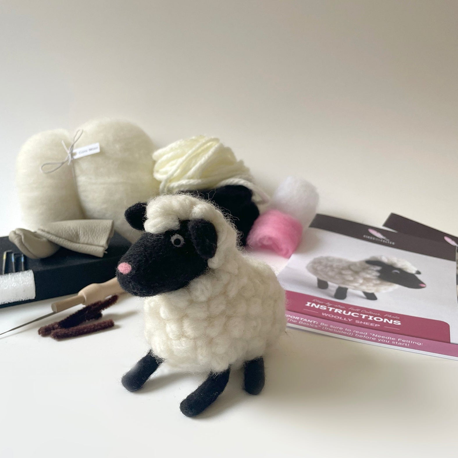 Knitted sheep toy with yarn balls, knitting needles, and instructions on a white background